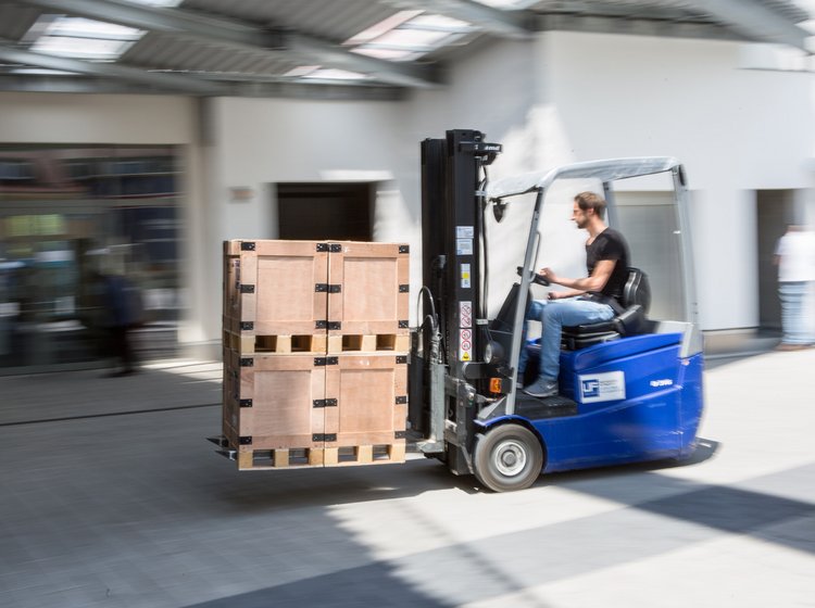 Ein Gabelstapler transportiert eine Palette mit Kartons durch eine Werkhalle.