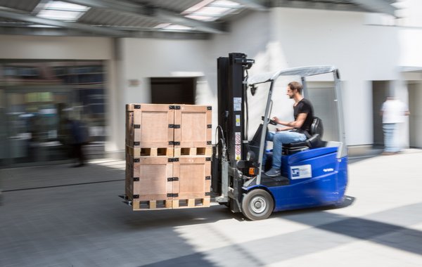 Ein Gabelstapler transportiert eine Palette mit Kartons durch eine Werkhalle.
