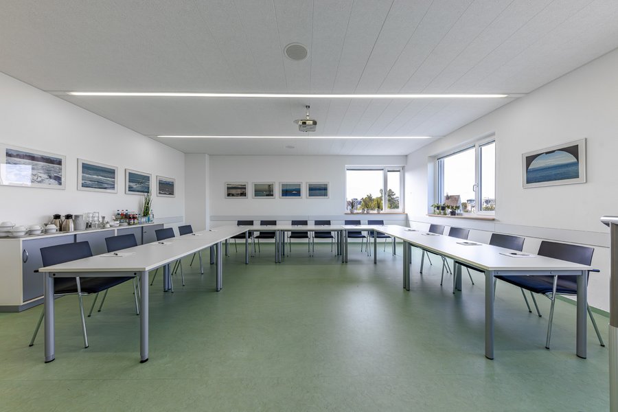 Großer Tagungsraum mit U-förmigen Tischen, Präsentationstechnik und Fensterfront.