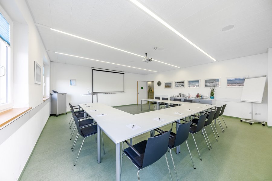 Tagungsraum mit U-förmiger Bestuhlung, Projektionsfläche und großen Fenstern.