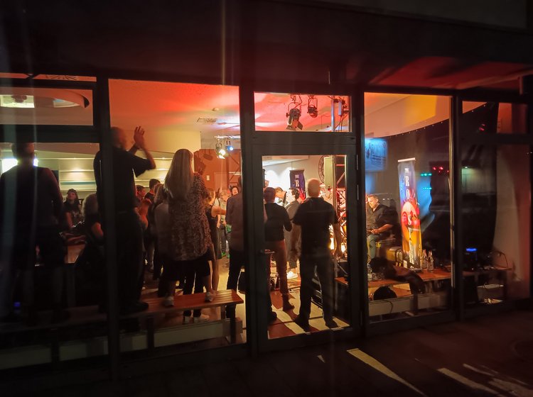 Menschen stehen abends vor einem beleuchteten Veranstaltungsraum.