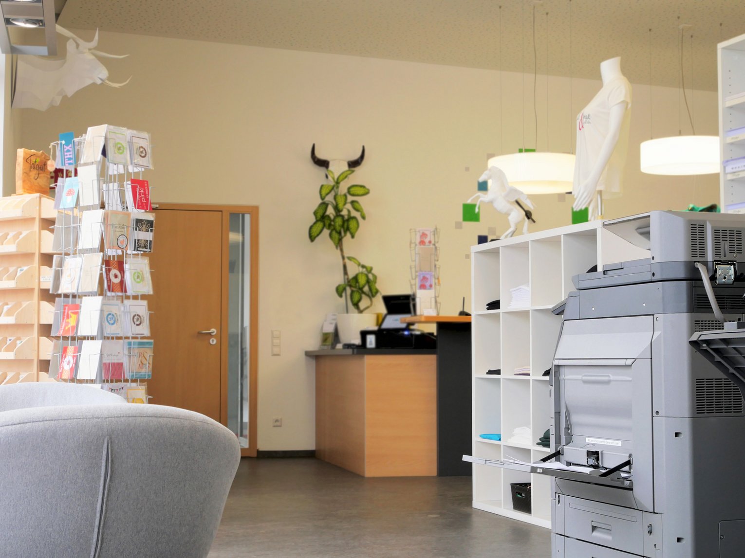 Heller Arbeitsraum mit Regalen, Drucker und sortierten Materialien.