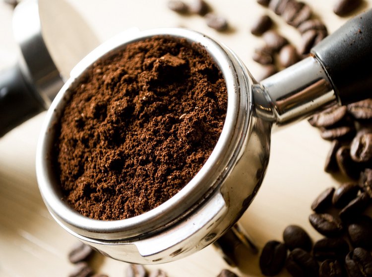 Frisch gemahlenes Kaffeepulver in einem Siebträger zwischen Kaffeebohnen.