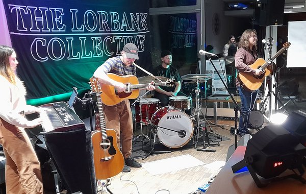 Eine Band mit Gitarren, Keyboard und Schlagzeug spielt auf einer kleinen Bühne.