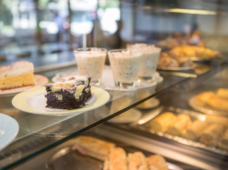 Kuchenstücke und Desserts liegen in einer beleuchteten Verkaufsvitrine.