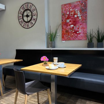 Kleine Sitzecke mit Tisch, schwarzer Bank und farbigem Wandbild.