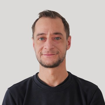 Mann mit kurzem Haar und schwarzem Oberteil vor hellem Hintergrund.